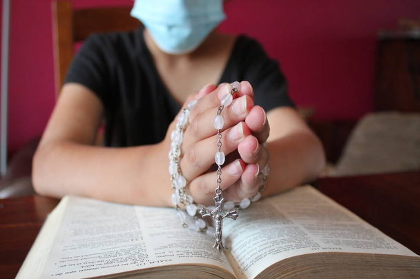 Katolickie ręce modlące się z biblijnym i różańcowym tle paciorków z maską koronawirusową - Zdjęcie, obraz