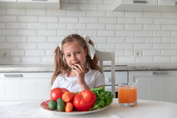 little girl eats vegetables in the kitchen. healthy food. vegetarianism. Copy space - Φωτογραφία, εικόνα