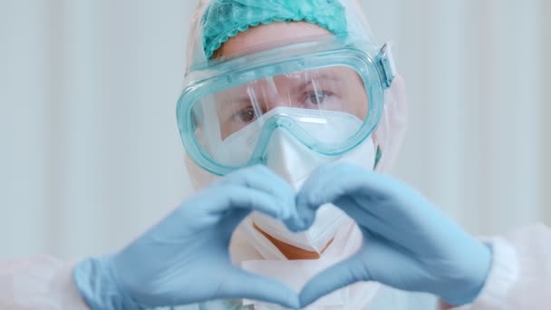 Close up of a doctor in a protective medical suit shows a heart folded from his hands. - Séquence, vidéo