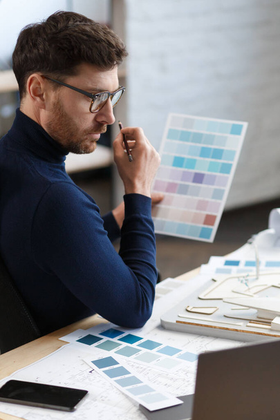Architect working in office with color palette. Engineer select colors for building using color swatches, searching new ideas for construction project. Portrait of handsome bearded man at workplace - Fotó, kép