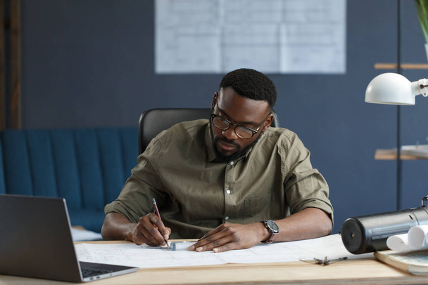 Afro-American architect working in office with blueprints.Engineer inspect architectural plan, sketching a construction project. Portrait of black handsome man sitting at workplace. Business concept - Foto, Imagem