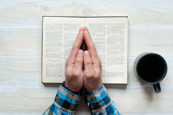 Open Holy Bible. Hands folded in prayer. Cup on a wooden background. - Foto, imagen