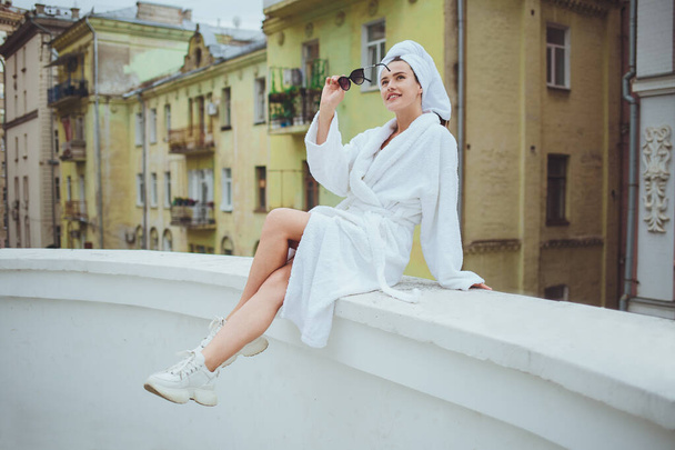 Beautiful young smiling girl in a white robe on the balcony - Foto, immagini