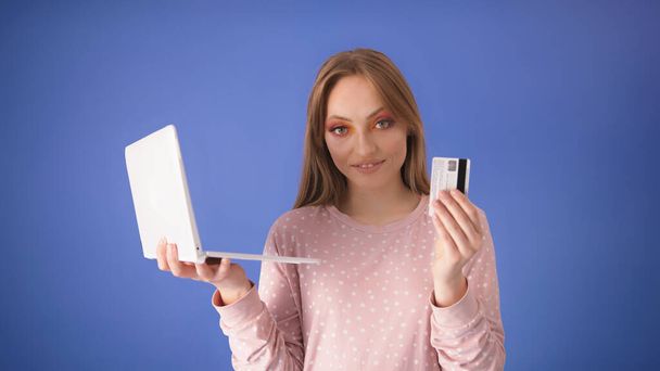 ラップトップとクレジットカードを持っている大きな笑顔を持つ若い白人女性。オンラインショッピングのコンセプト - 写真・画像