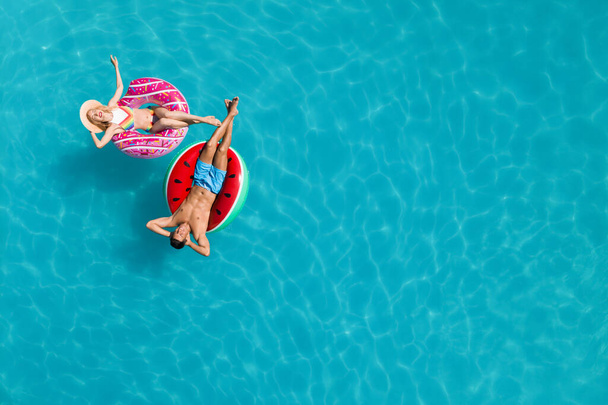 Happy couple with inflatable rings in swimming pool, top view and space for text. Summer vacation - Φωτογραφία, εικόνα