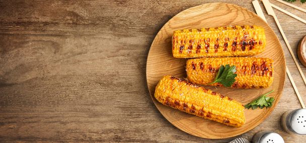 Delicious grilled corn cobs and space for text on wooden table, flat lay. Banner design - Zdjęcie, obraz