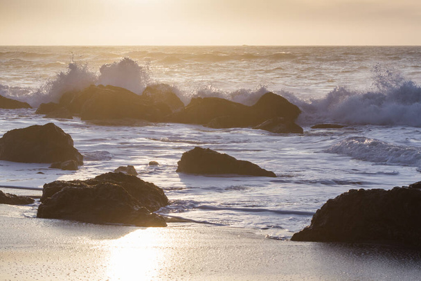 Скелястий берег на пляжі Несіка, штат Орегон, пізно пополудні, коли сонце наближається до обрію і хвилі врізаються в скелі. - Фото, зображення