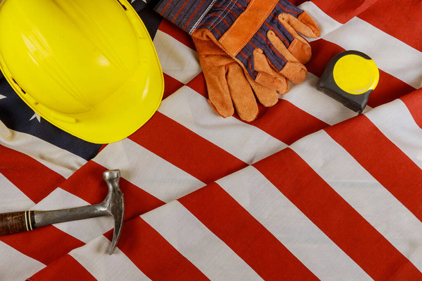 Πρωτομαγιά κατασκευή κίτρινο κράνος εργαλεία εξοπλισμού για την εργασία ευτυχισμένη ομοσπονδιακή αργία πάνω από αμερικανική σημαία φόντο. - Φωτογραφία, εικόνα