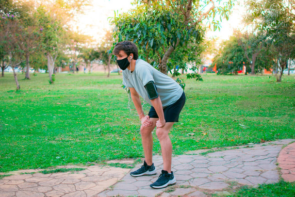 Un giovane uomo con una maschera dall'aspetto stanco dopo essersi allenato nel parco. - Foto, immagini