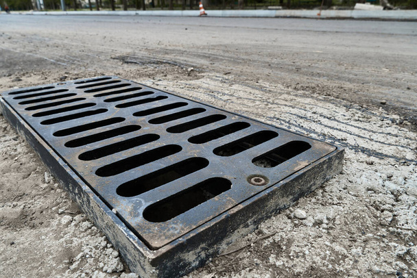 Новая дождевая решетка на дороге или тротуаре, установка в бетоне. Канализационная система города для осушения воды во время сильных дождей - Фото, изображение