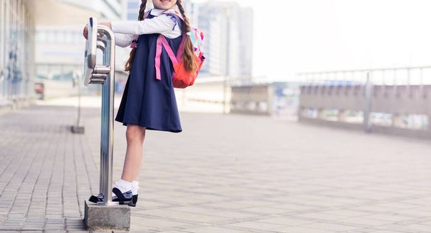 Дівчина в синій шкільній сукні і рожевий рюкзак на спині. Горизонтальна фотографія
 - Фото, зображення