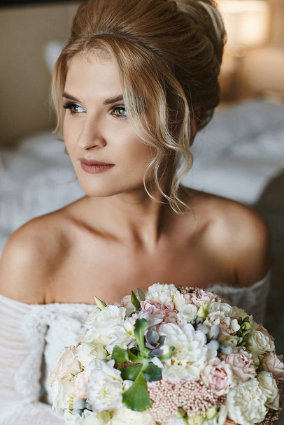 Portrait of a young woman with bridal coiffure and in a wedding gown with a bridal bouquet in her hands - Photo, Image