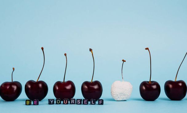 Inscription "be yourself", composed of small letters-beads background of berries of cherries standing in formation, one of which is painted in white. Focus on letters. Freedom concept - Photo, Image