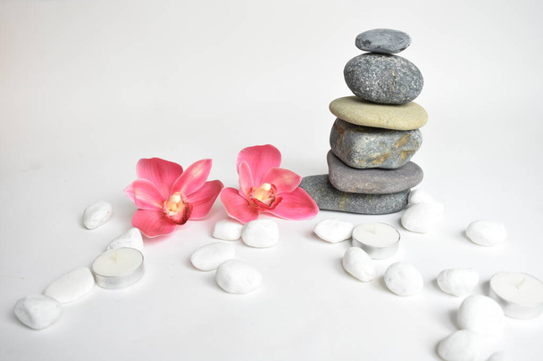 Stack stones isolated in white background and pink orchid flower. Pebbles tower. Concept of balance and harmony. Calm and spirit, spa stones and zen, peace, meditation, spiritual, abstract - Photo, Image