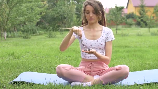 Mladá krásná dívka s dlouhými dredy drží v ruce náhrdelník z přírodních kamenů pro meditaci venku během dopoledne na zelené trávě svého dvorku - Záběry, video