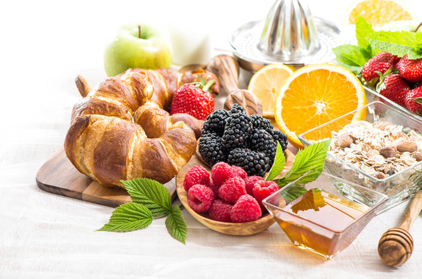 Healthy food. Breakfast table with fresh berries, fruits, honey, croissant, muesli - Foto, afbeelding