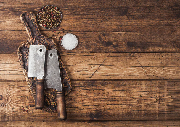 Vintage hatchets for meat on wooden chopping board with salt and pepper on wooden background. - Zdjęcie, obraz