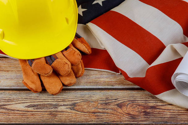 Κατασκευή κίτρινο κράνος και δερμάτινα γάντια για ευτυχισμένη Ημέρα Εργασίας ΗΠΑ μια ομοσπονδιακή αργία των Ηνωμένων Πολιτειών Αμερικής Σημαία πατριωτικό φόντο ξύλο - Φωτογραφία, εικόνα