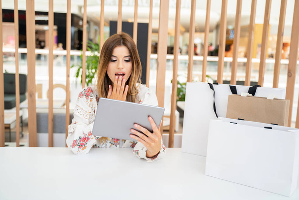 Attractive smiling girl with happy expression on her face doing online shopping on tablet. Seasonal sale time. - Foto, afbeelding