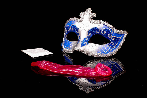 Sexy blauw erotisch gezicht masker en roze gebruikt condoom geïsoleerd op de zwarte reflecterende achtergrond - Foto, afbeelding