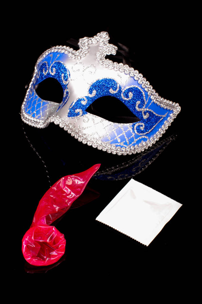 Seksi mavi erotik yüz maskesi ve siyah yansıtıcı arka planda izole edilmiş pembe prezervatif. - Fotoğraf, Görsel