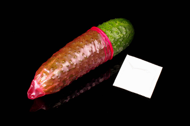 Roze condoom op de grote groene komkommer. Het begrip seksuele opvoeding - Foto, afbeelding