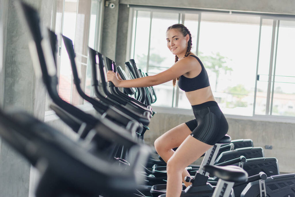 Athlete, woman, girl exercising, biking in the gym. She wears sports clothes to exercise. - Foto, Bild