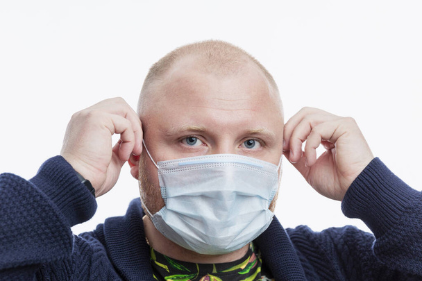 A bald man puts on a medical mask. Close-up. Isolated on white background. Coronavirus pandemic. - Foto, Imagem
