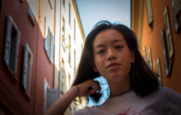 Ritratto di adolescente asiatico americano in piedi di fronte a vecchi edifici sorridenti - Foto, immagini