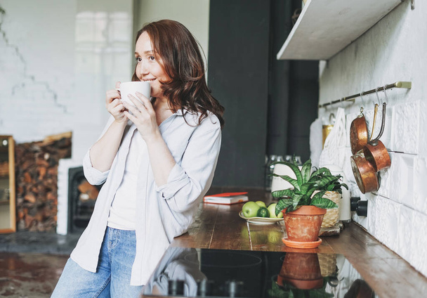 Erwachsene lächelnde brünette Frau in lässig mit Tasse Tee auf Küche zu Hause - Foto, Bild