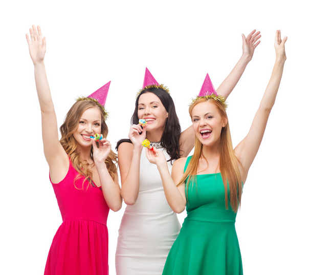 Three smiling women in hats blowing favor horns - Foto, Imagen