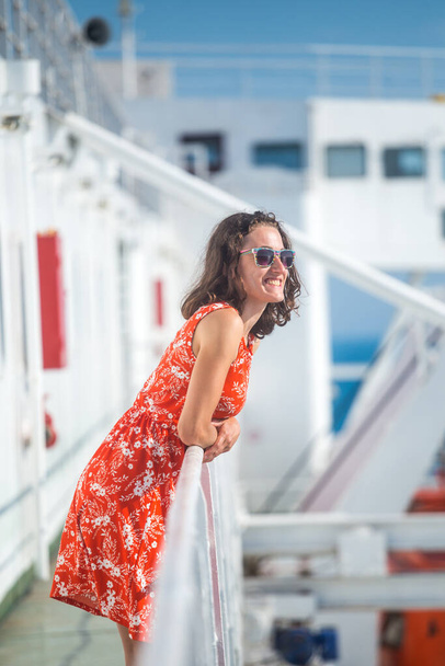 Uma mulher está navegando em um navio de cruzeiro, uma menina está de pé perto da cerca em um navio e olhando para o mar, viajando de balsa, uma morena em um vestido de verão admira o oceano. - Foto, Imagem