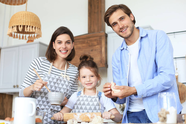 Cute little girl and her parents are having fun while cooking in kitchen at home together - Φωτογραφία, εικόνα