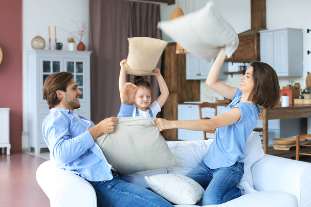 Happy young family having fun with pillows on sofa - Fotoğraf, Görsel