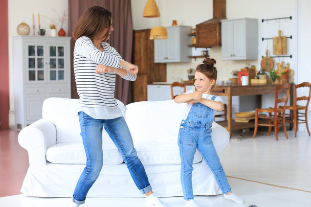 Cheerful mother with little daughter dancing at favourite song in living room at home - Foto, Bild