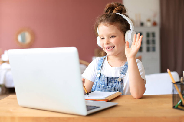 Distance learning. Cheerful little girl girl in headphones using laptop studying through online e-learning system. - Fotó, kép