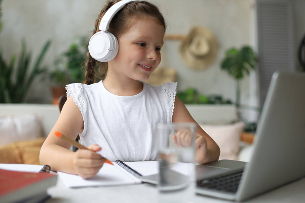 Distance learning. Cheerful little girl girl in headphones using laptop studying through online e-learning system - Valokuva, kuva