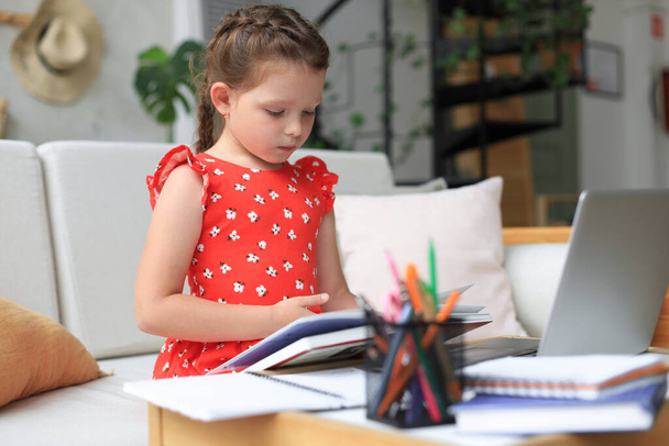 Little girl sits at the desl at home and does homework, self study of the material, reading book. The concept of distance education - Zdjęcie, obraz
