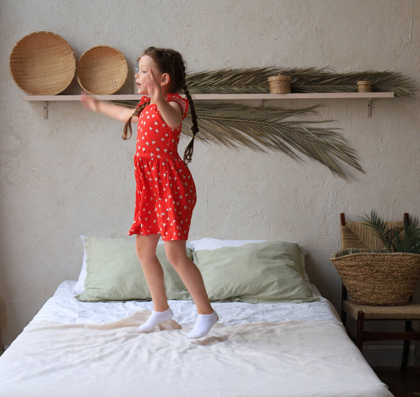 Happy little girl jumping on bed, singing a song - Фото, изображение
