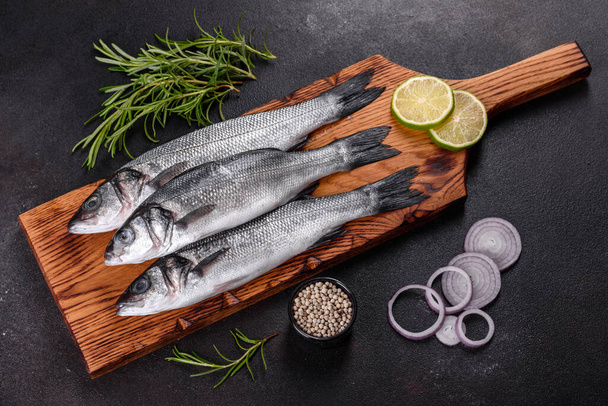 Verse vis zeebaars en ingrediënten voor het koken. Rauwe vis zeebaars met specerijen en kruiden op een donkere tafel - Foto, afbeelding