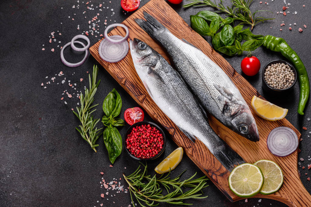 Fresh fish seabass and ingredients for cooking. Raw fish seabass with spices and herbs on a dark table - 写真・画像