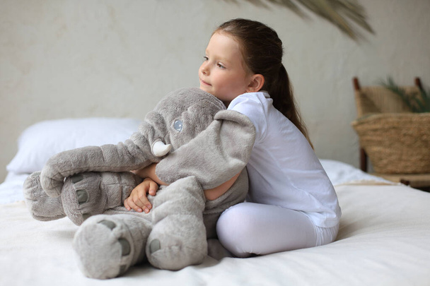 Sweet little girl sitting on her bed at home with toy elephant - Fotoğraf, Görsel