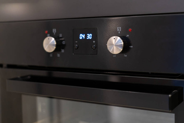 家電製品の組み込みを閉じます。モダンなキッチンルームのコントロールパネル上のタイマーとボタン付き電気オーブンの要素 - 写真・画像