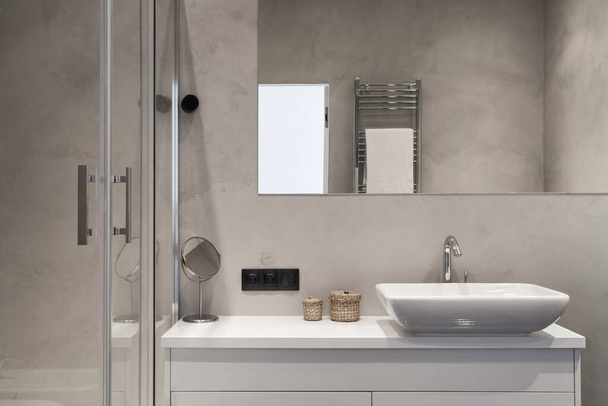 Prvek moderního domu s moderním interiérovým designem v koupelně, sprchovací kout, zrcadlo nad umyvadlem na desce pultu a vyhřívaná zábradlí proti šedé stěně - Fotografie, Obrázek