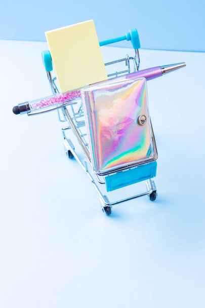 Shopping cart with school supply. School notepad with holographic cover. Stationery in shopping trolley. Back to school concept - Foto, immagini
