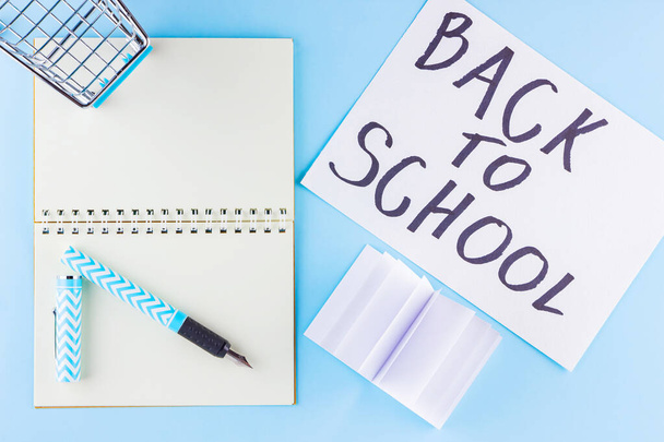 Back to school concept. Shopping cart and stationery on blue background. Pen, notepad and shopping trolley. Time to study. Top view - Foto, imagen