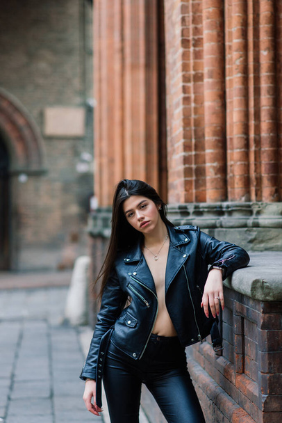 Portret pięknej młodej brunetki w stylowej czarnej skórzanej kurtce, uśmiecha się na miejskim tle, szczęśliwy czas, Travel Concept. - Zdjęcie, obraz
