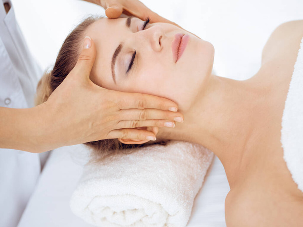 Young and blonde woman enjoying facial massage in spa salon. Beauty concept - Photo, Image