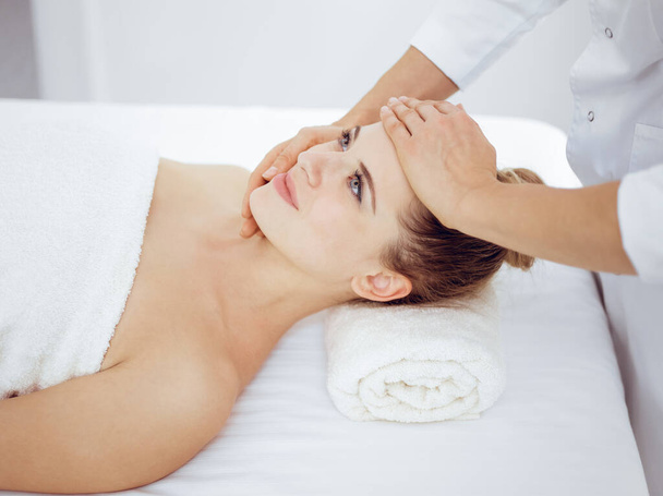 Young and blonde woman enjoying facial massage in spa salon. Beauty concept - Фото, зображення