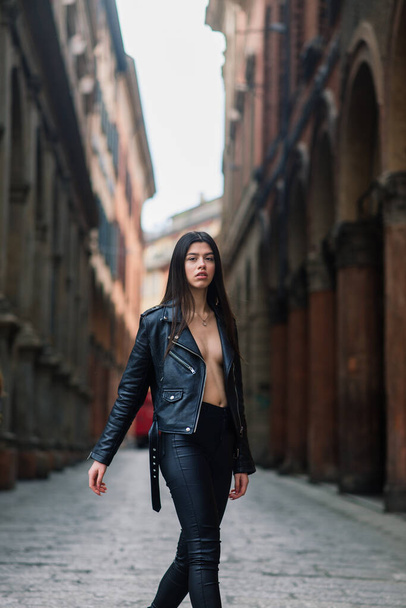 Retrato de bela jovem morena vestindo casaco de couro preto elegante, ela sorrindo no fundo urbano, tempo feliz, conceito de viagem. - Foto, Imagem